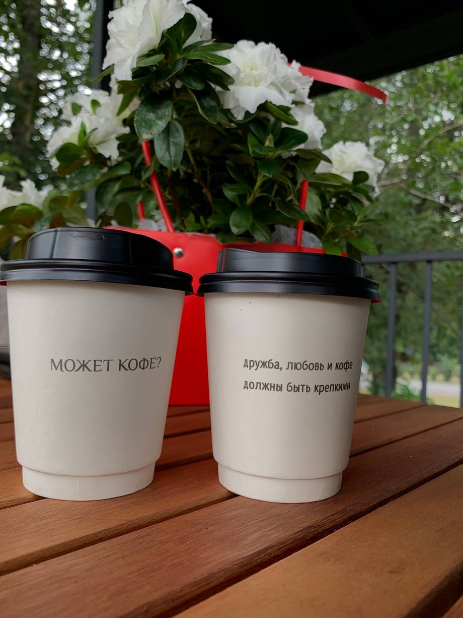 Coffee cups with branded Cyrillic text and white flowers in outdoor setting