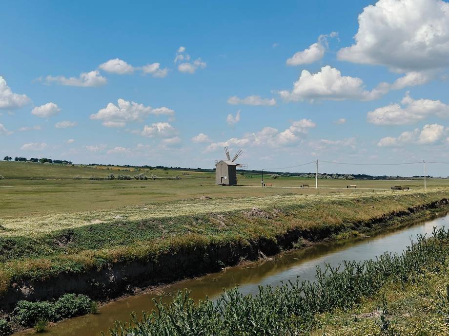 Rural agricultural landscape with irrigation canal and distant windmill
