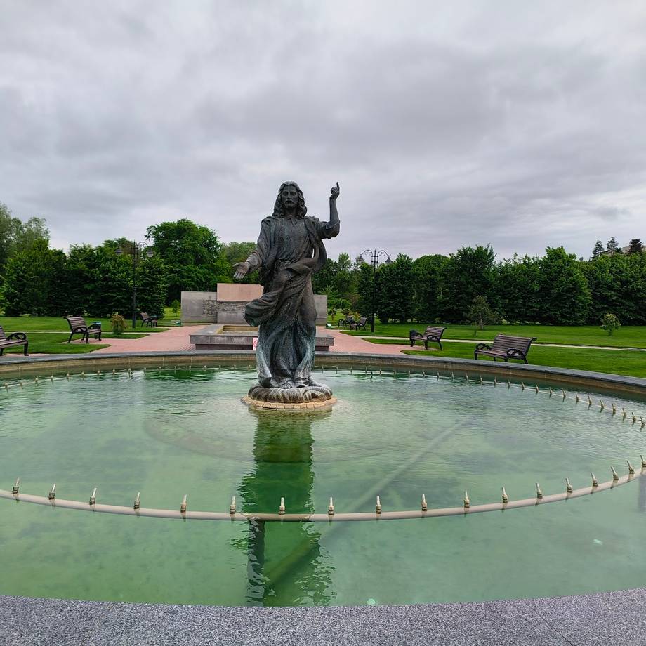 Iconic statue fountain in manicured garden with pond and tree-lined grounds