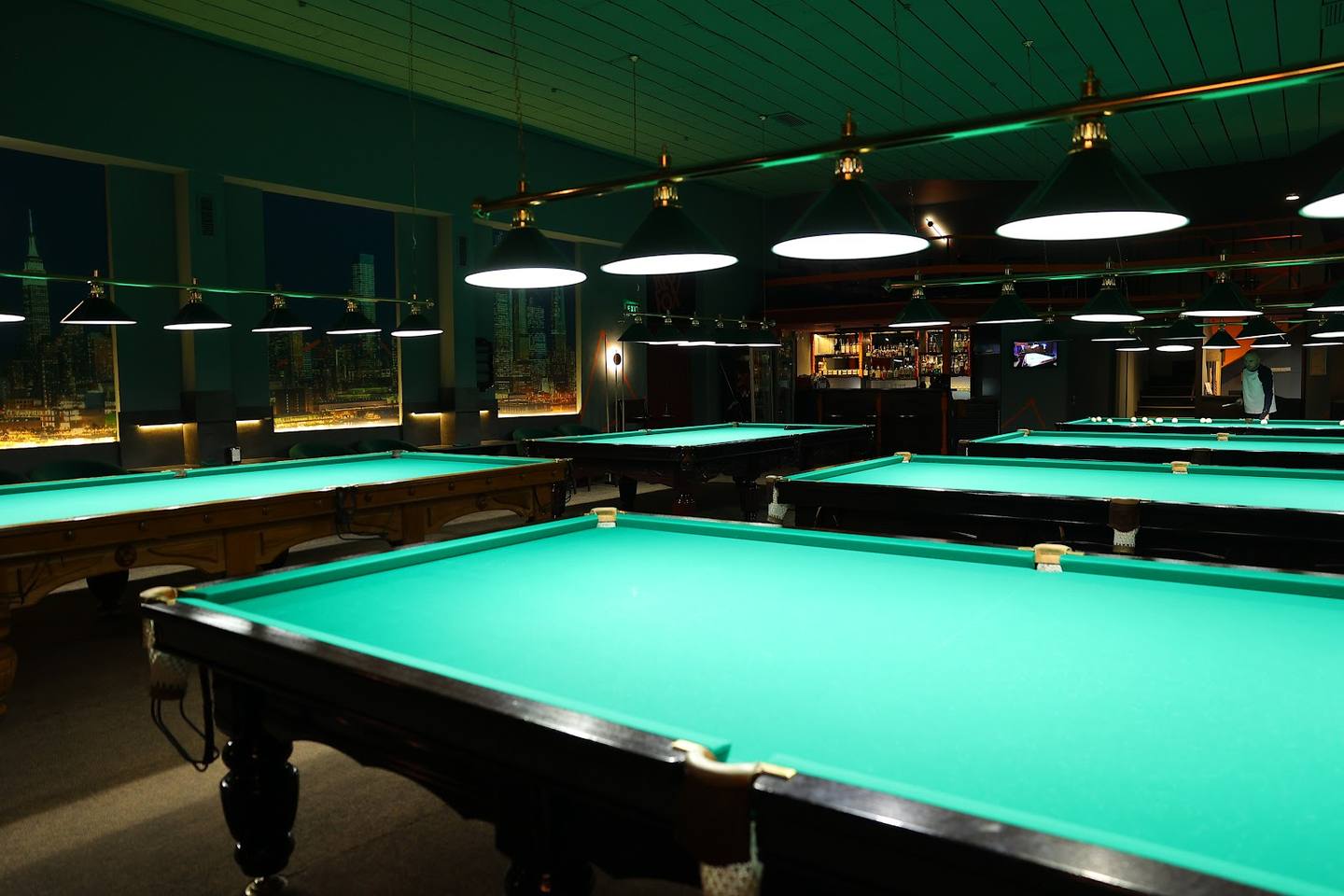 Billiards hall with multiple pool tables under professional lighting and green interior