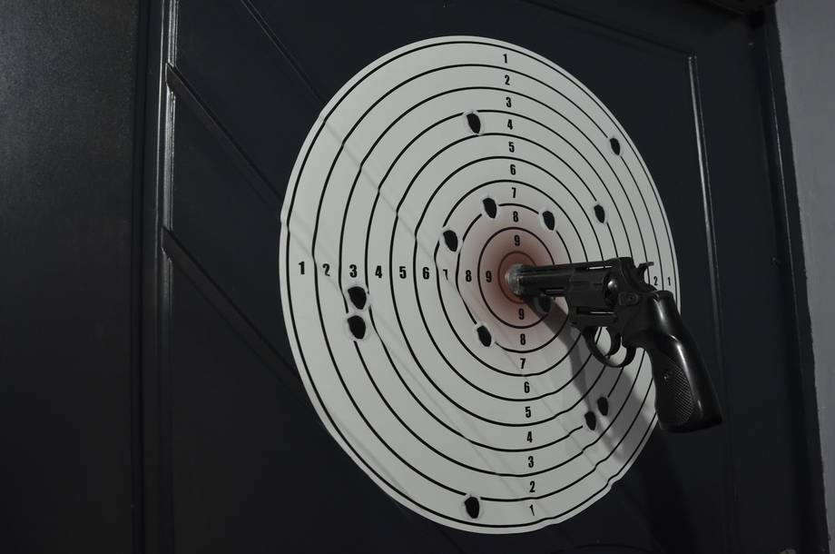 Air pistol pointed at shooting range target with bullet holes
