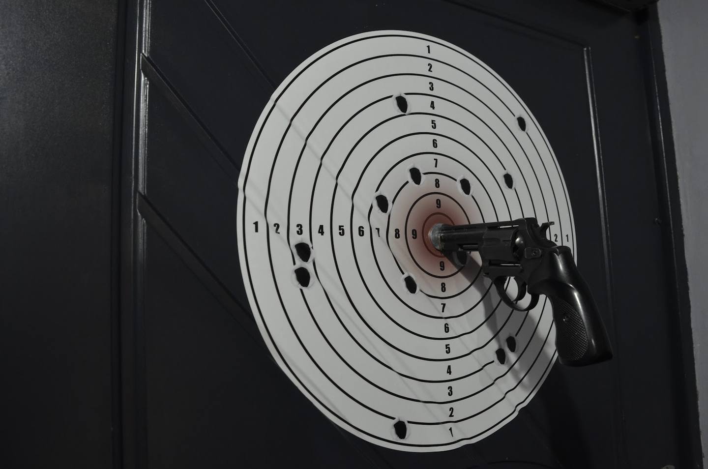 Air pistol pointed at shooting range target with bullet holes