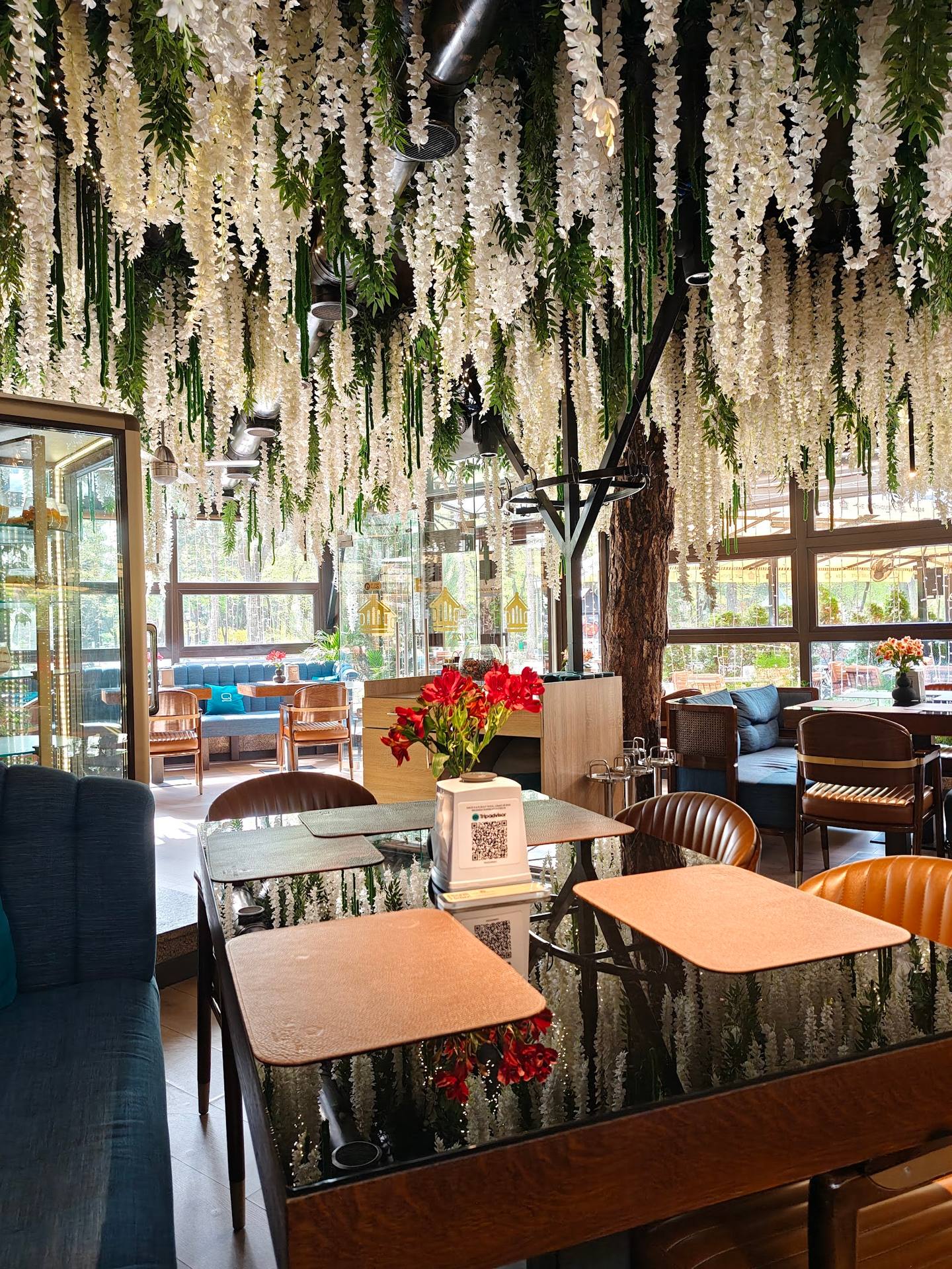 Modern cafe interior with dramatic cascading white floral installation above wooden seating area and natural light