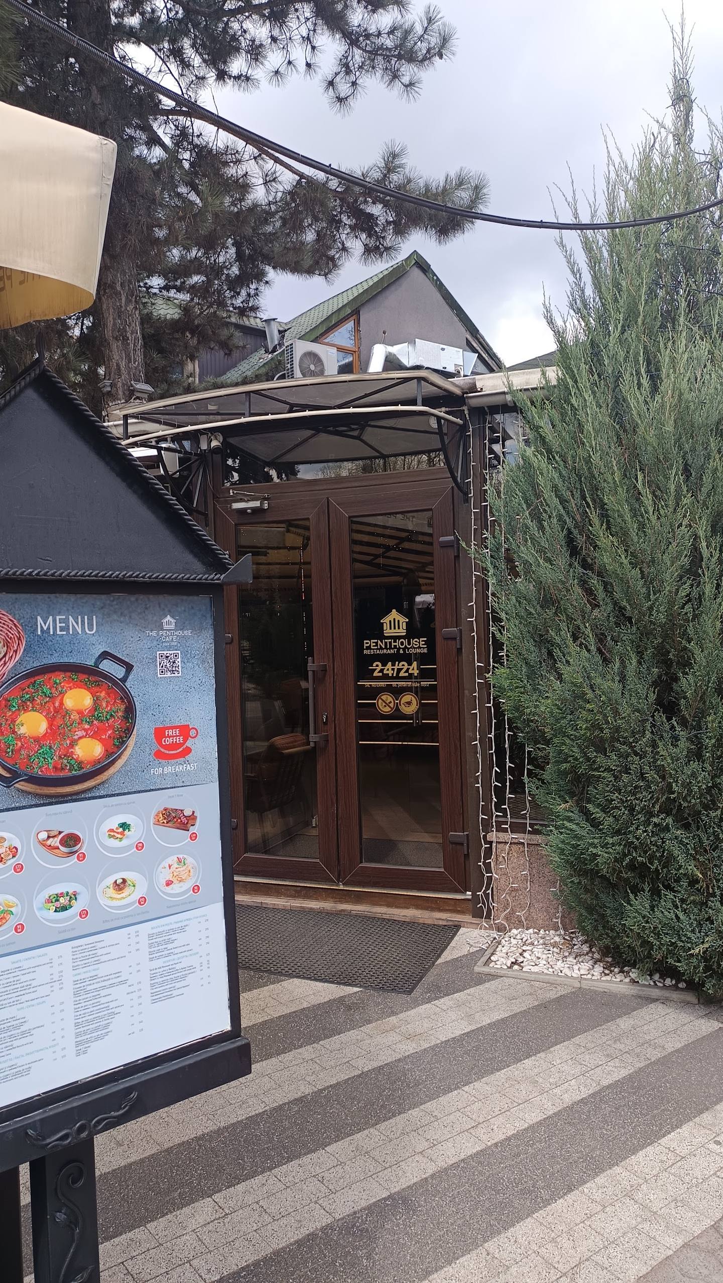 Restaurant storefront with dark wood entrance, menu board, and landscaped exterior