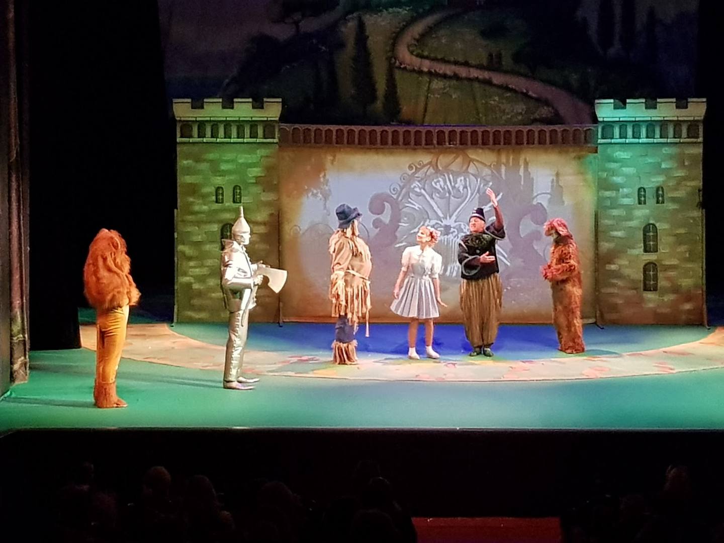 Theater stage performance with actors in costume under colored lighting and castle backdrop