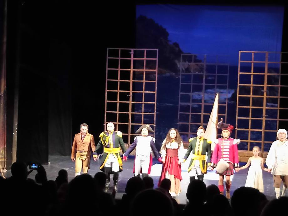 Theater performance with cast taking curtain call on lit stage