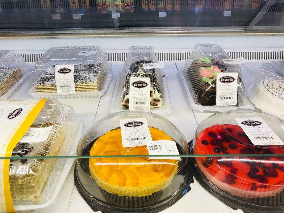 Refrigerated display of boxed cakes and desserts with yellow and red fruit toppings
