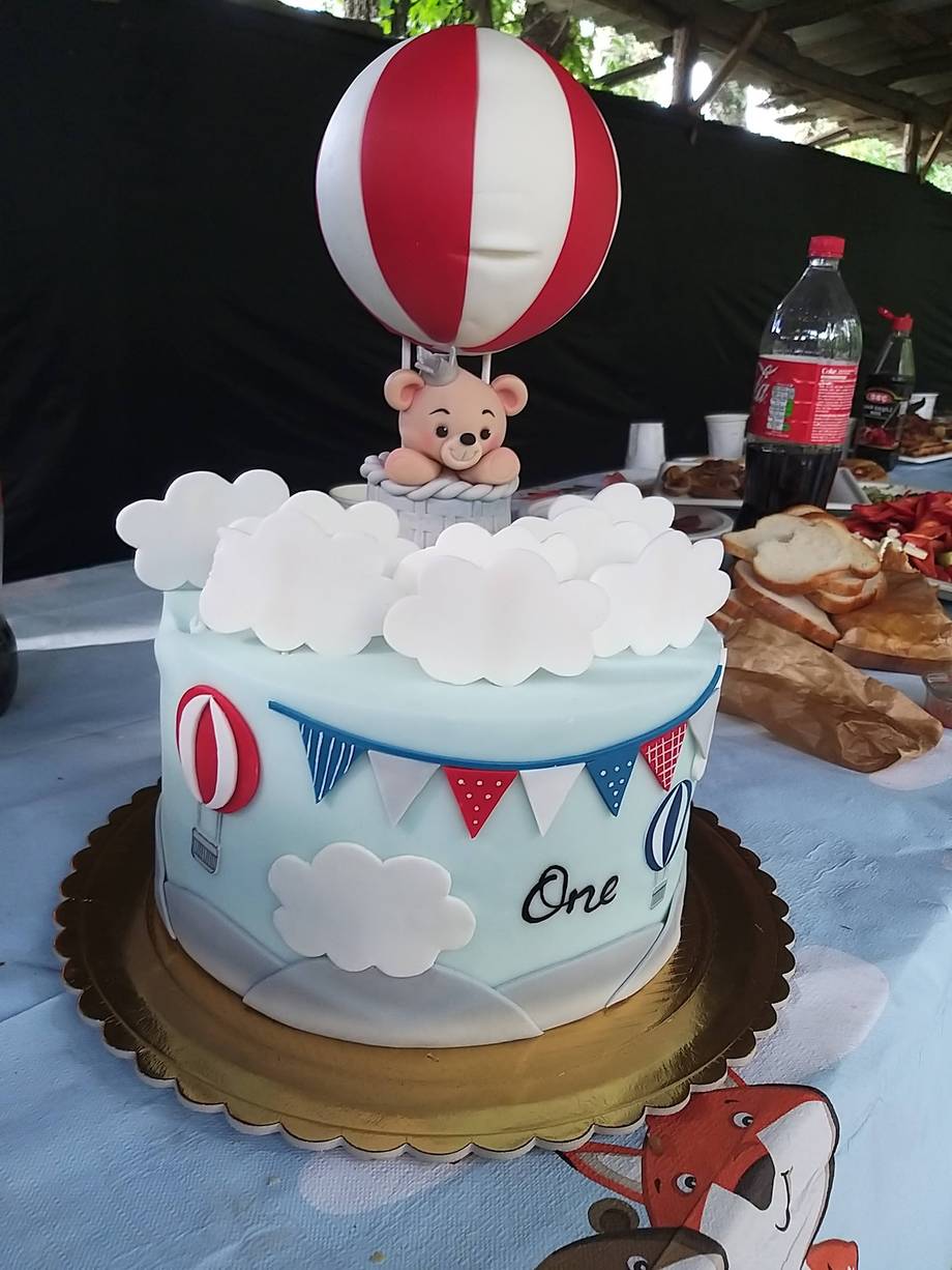 Hot air balloon themed cake with teddy bear topper and cloud decorations.