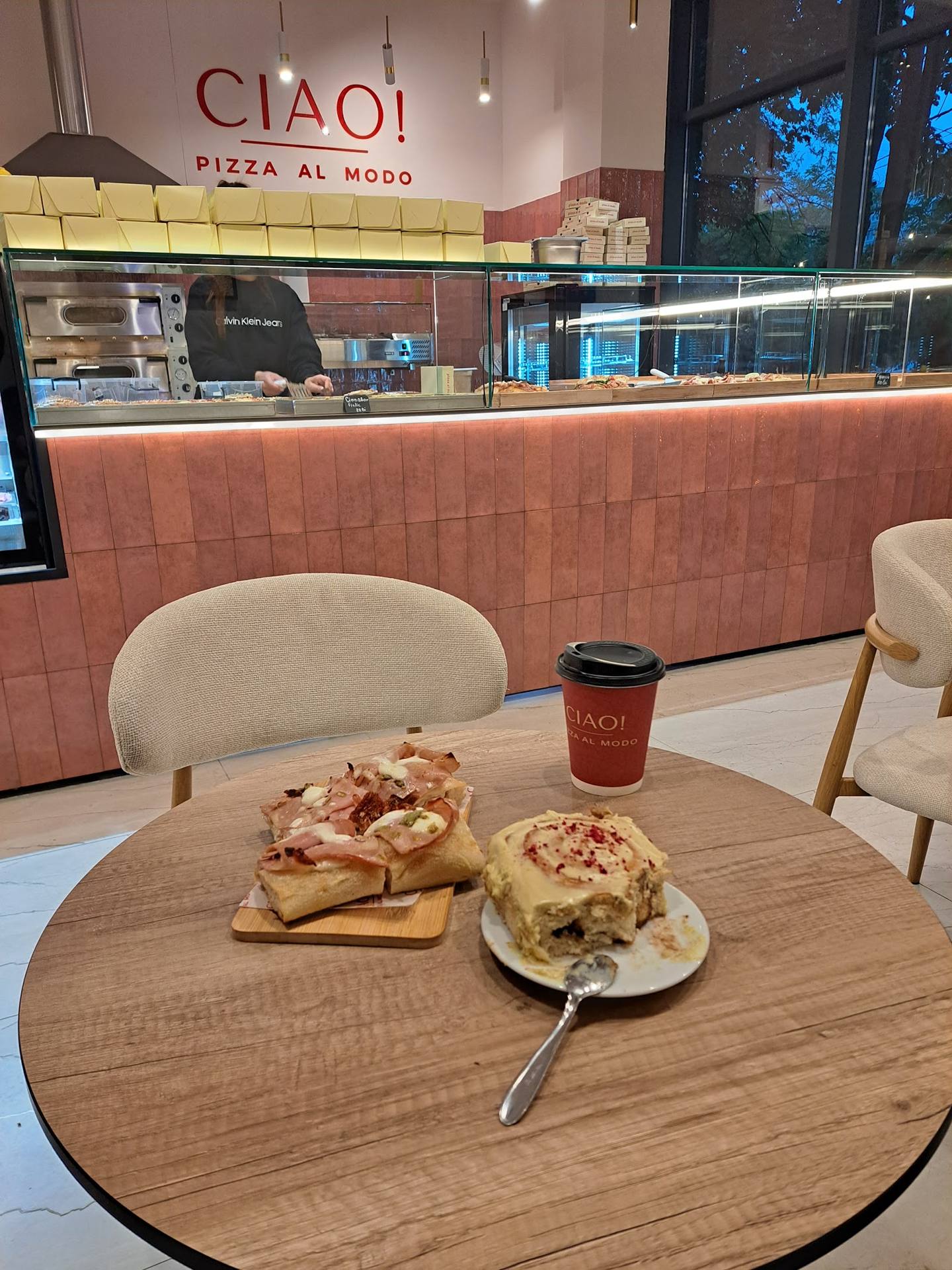 Modern pizza restaurant interior with wood tables, pink brick counter, and open kitchen view