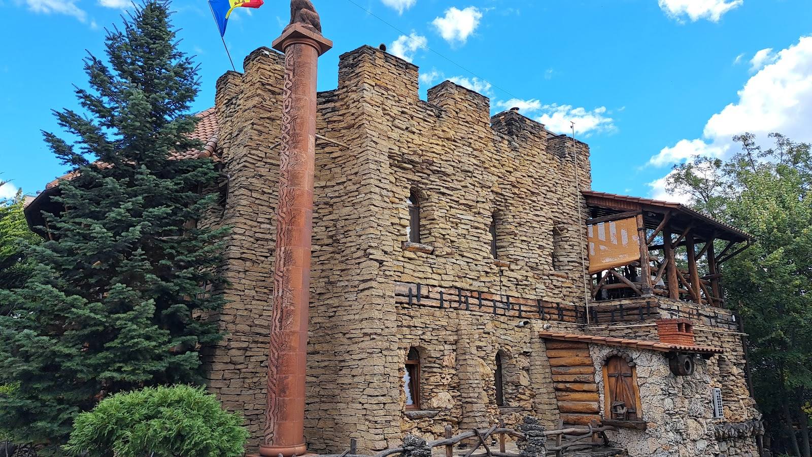 Historic stone fortress tower with brick chimney and wooden balcony, surrounded by evergreen trees.