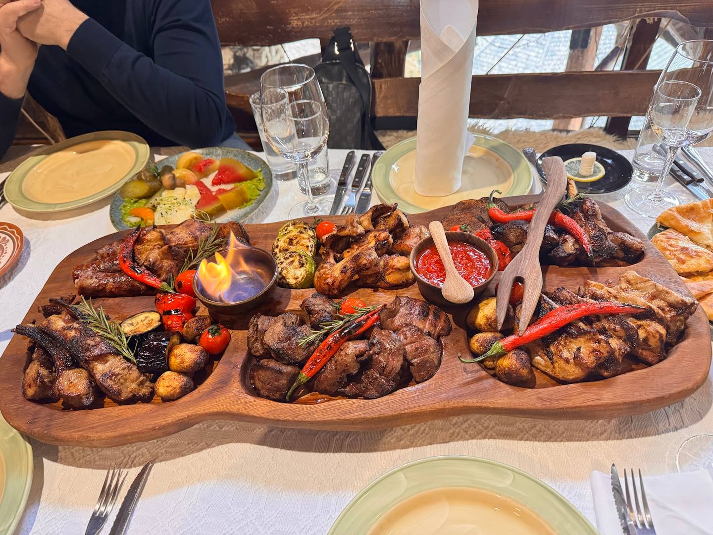 Mixed grilled meat and seafood platter on wooden board with table setting