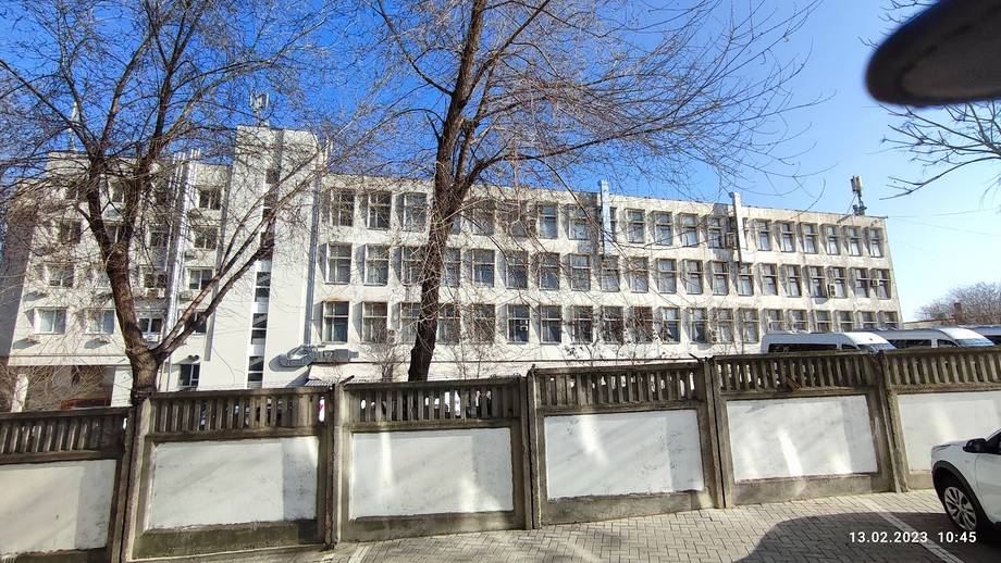 Multi-story Soviet-era institutional building with wooden fence perimeter, clear daytime exterior view