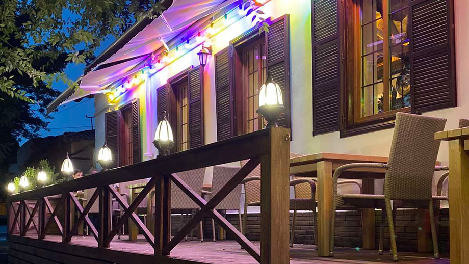 Evening exterior of restaurant with illuminated neo-classical facade and wooden deck seating