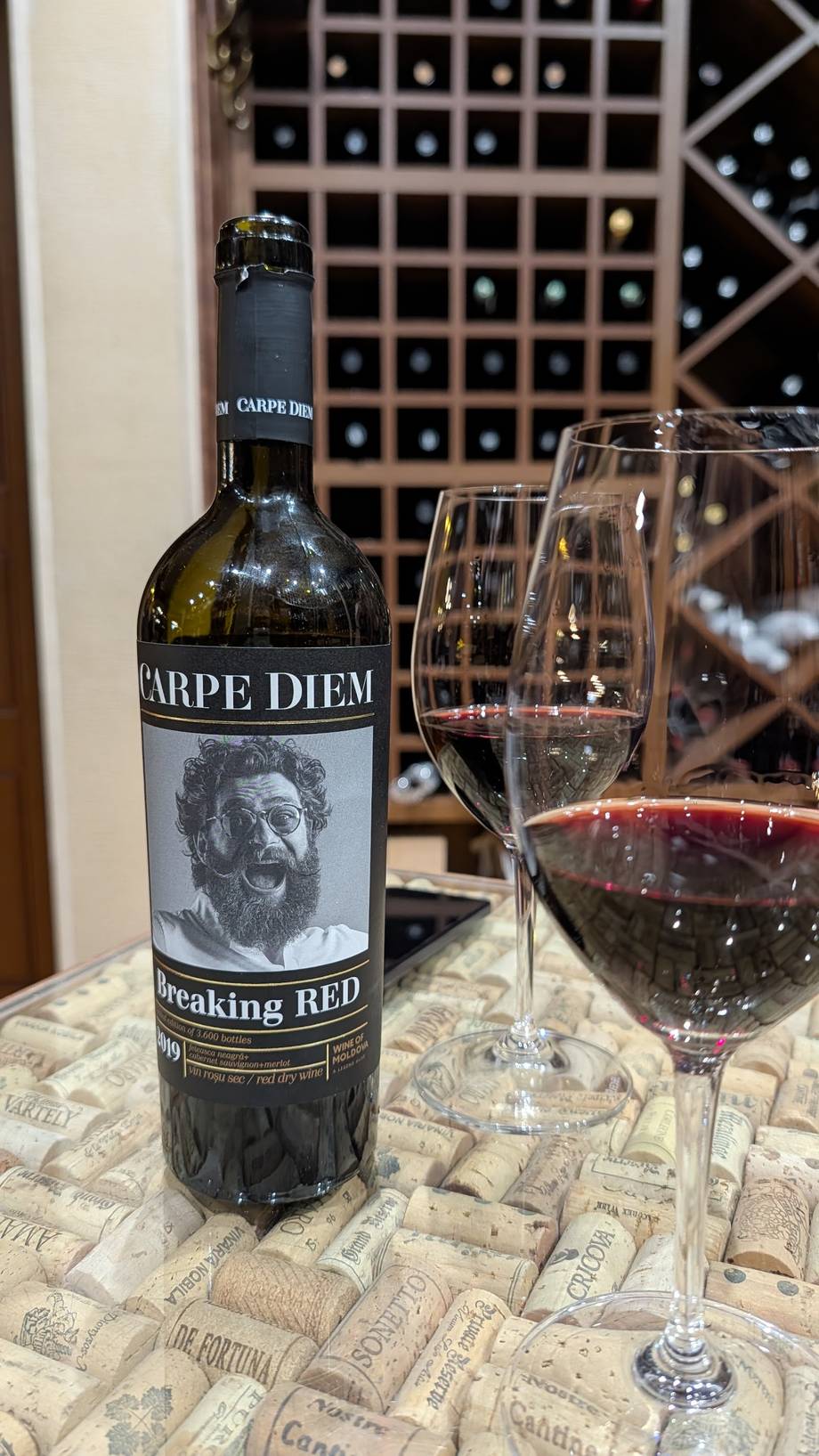 Carpe Diem Breaking Red wine with glasses displayed against wine cellar storage wall