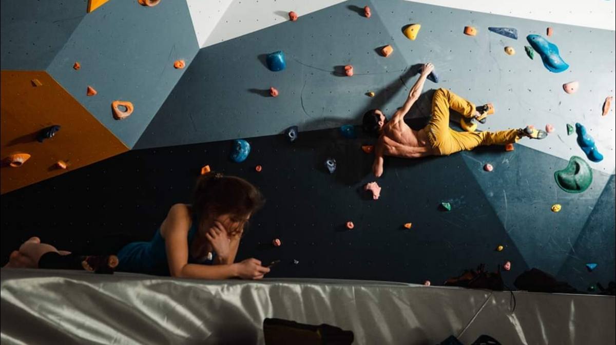 Two climbers on colorful holds ascending indoor climbing wall