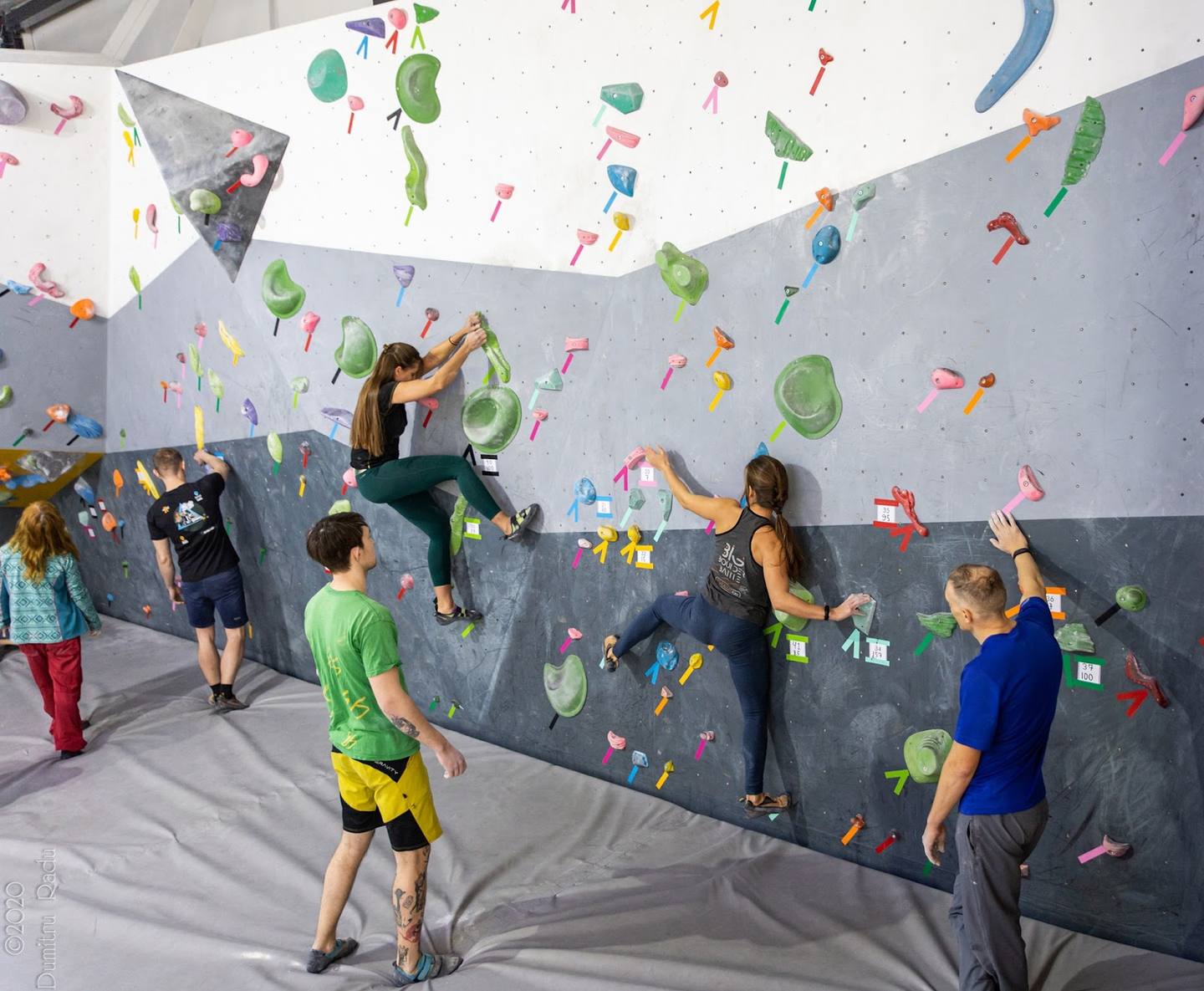 Indoor rock climbing wall with multiple climbers scaling colorful holds