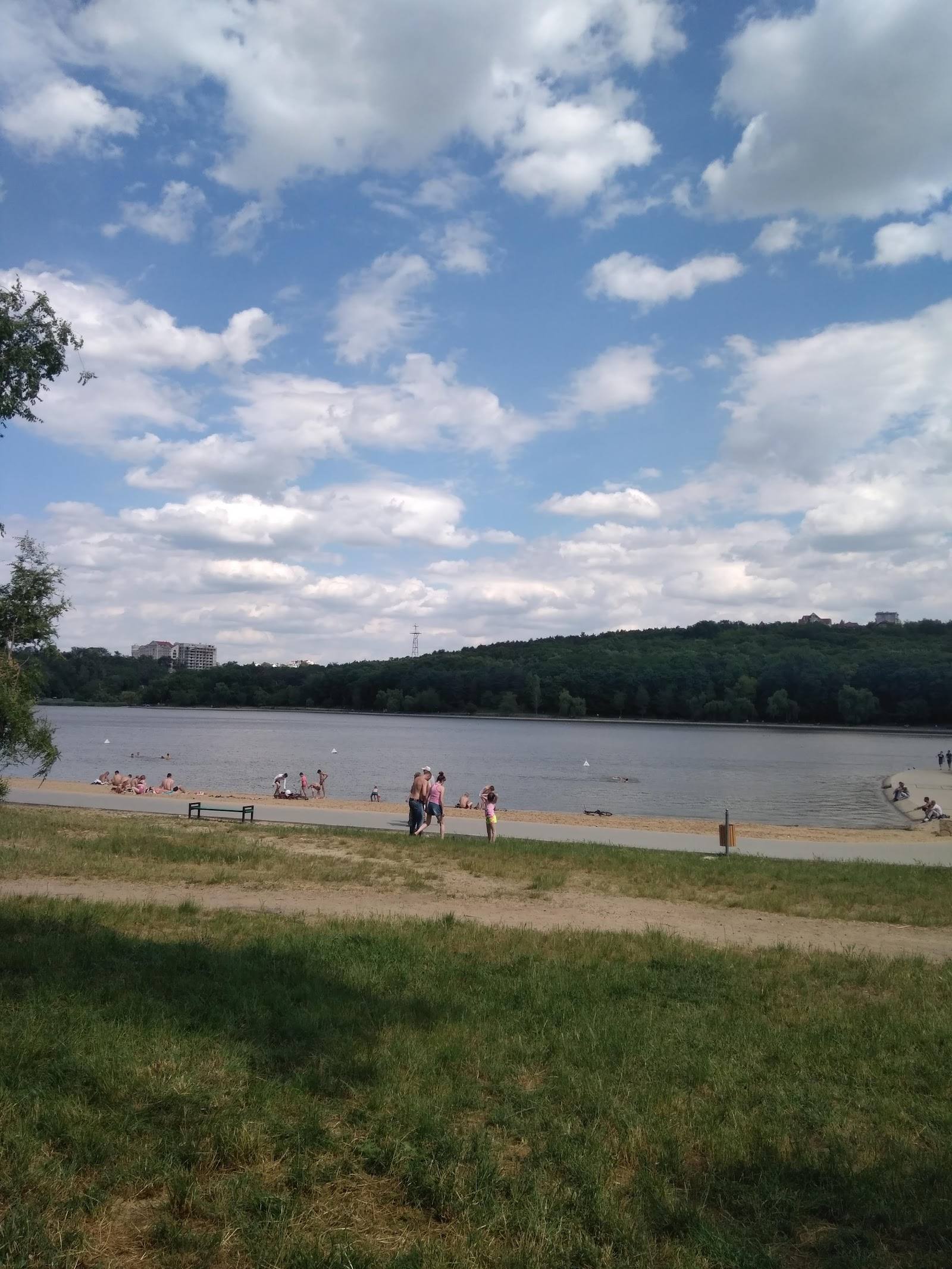 Scenic lake beach with swimming visitors and forested shoreline under clear sky