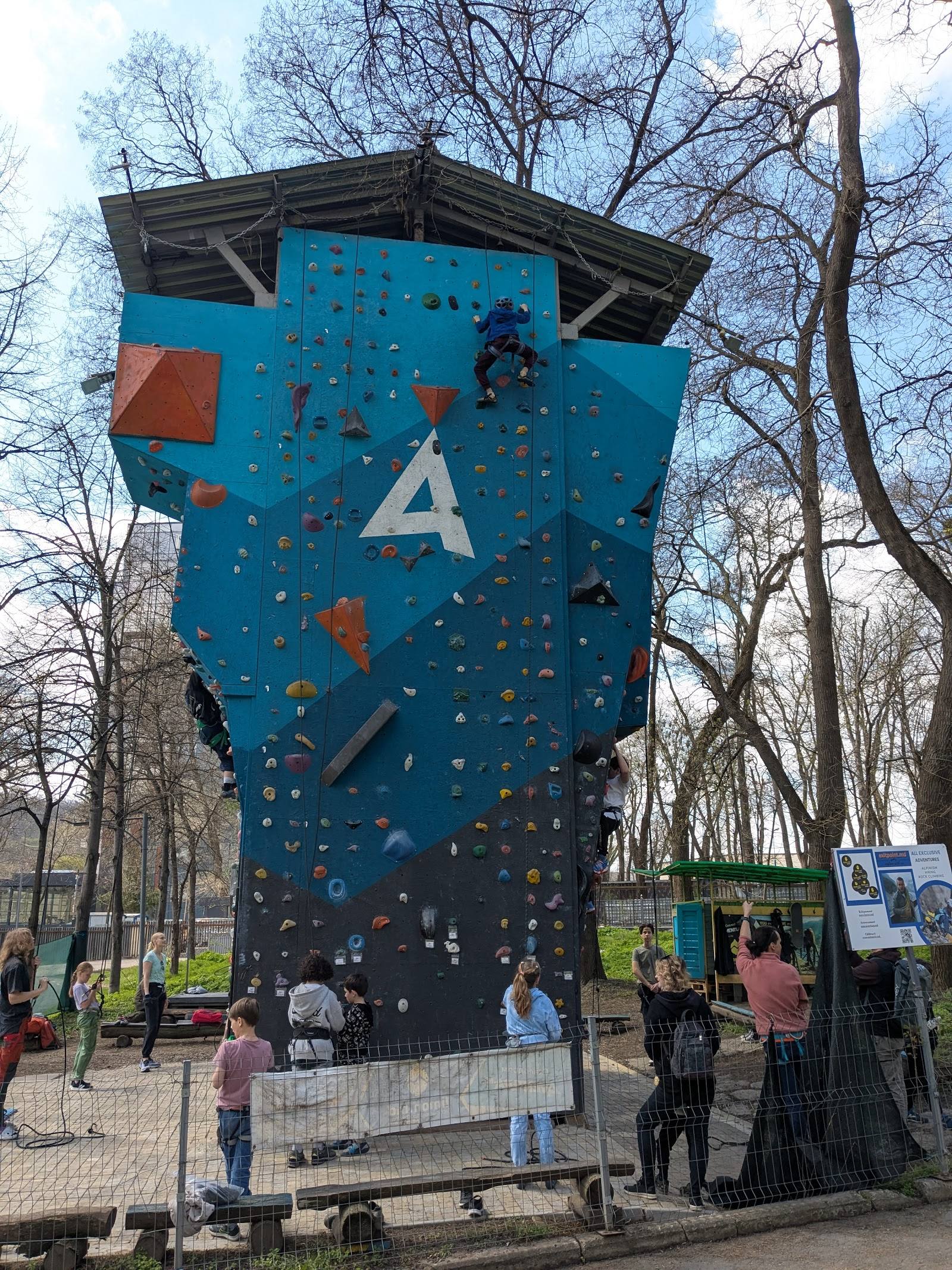 Tall blue climbing wall with marked route, outdoor activity venue with visitors