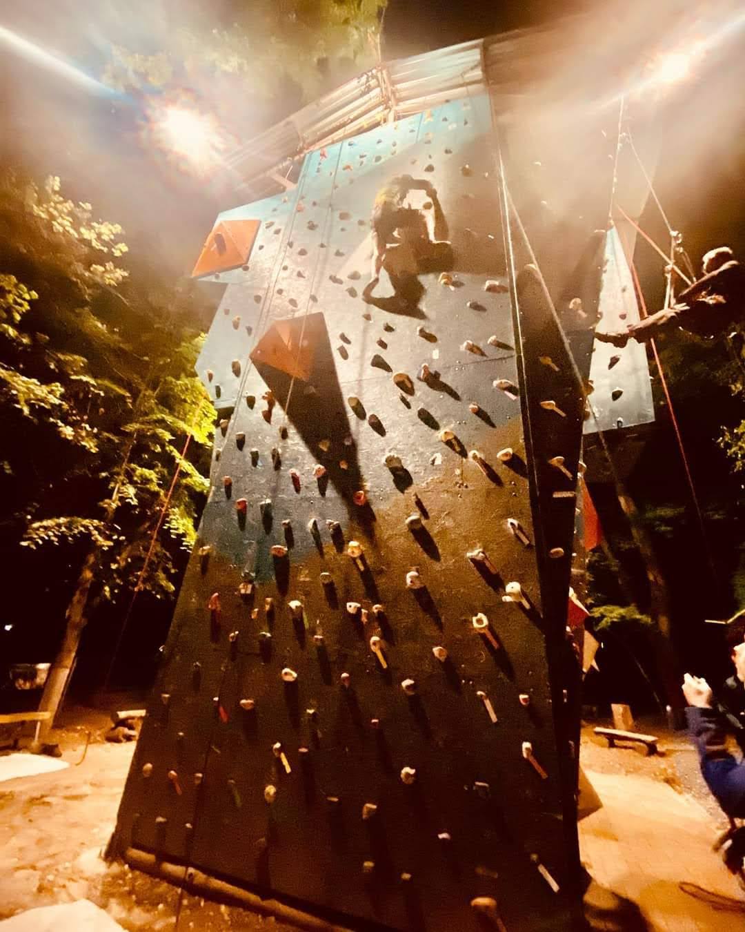 Rock climbing wall with climber at night, illuminated outdoor activity venue