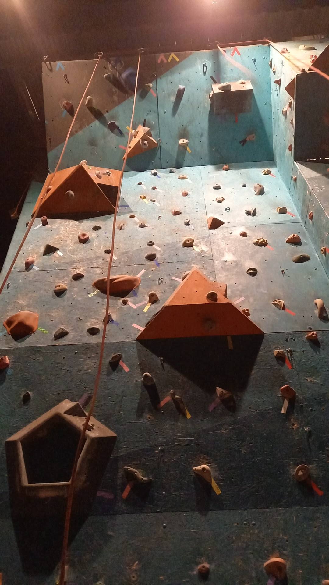Multi-panel indoor rock climbing wall with colored holds and roped sections