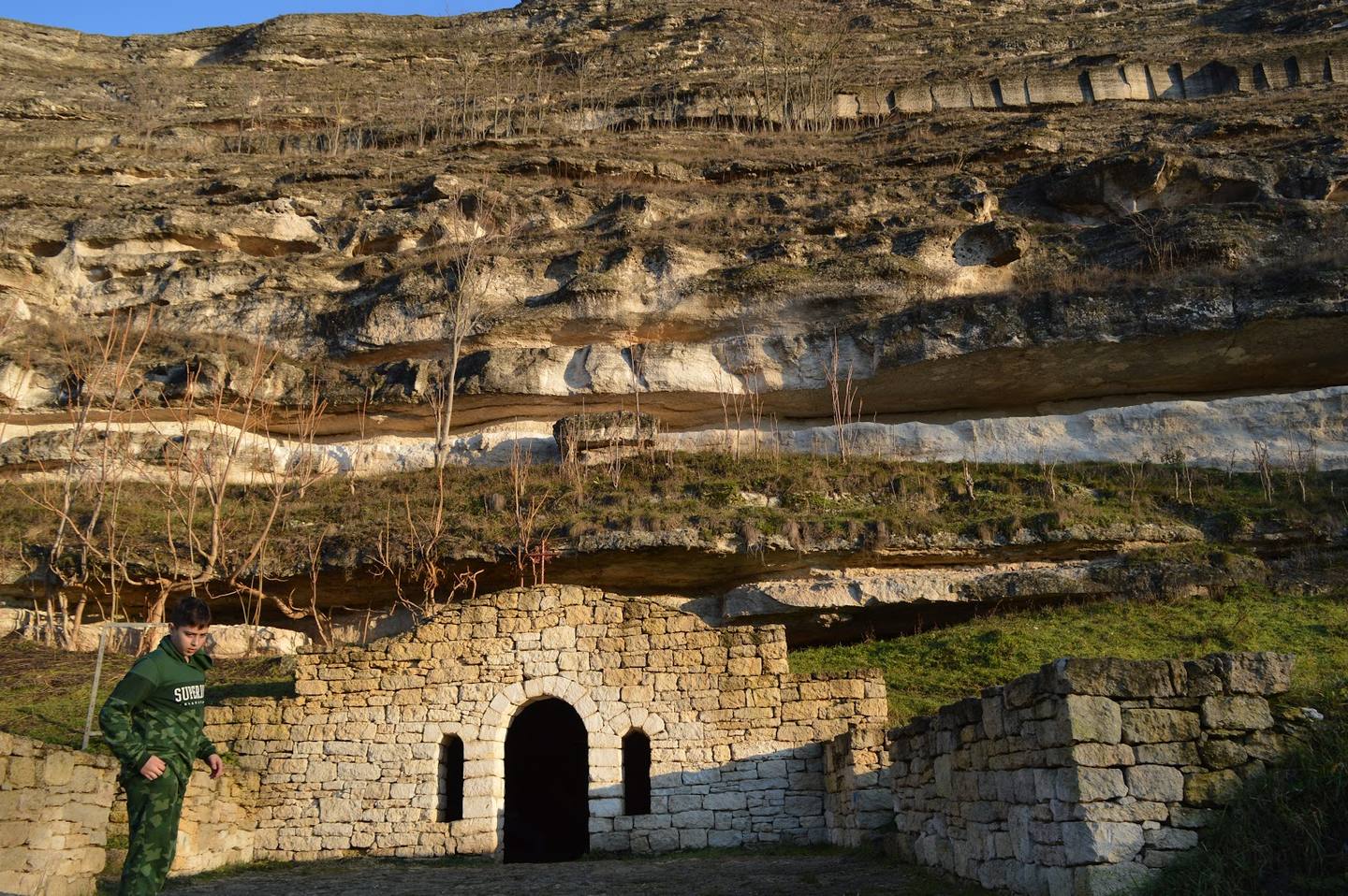 Stone monastery entrance with cliff face and vineyard terraces above
