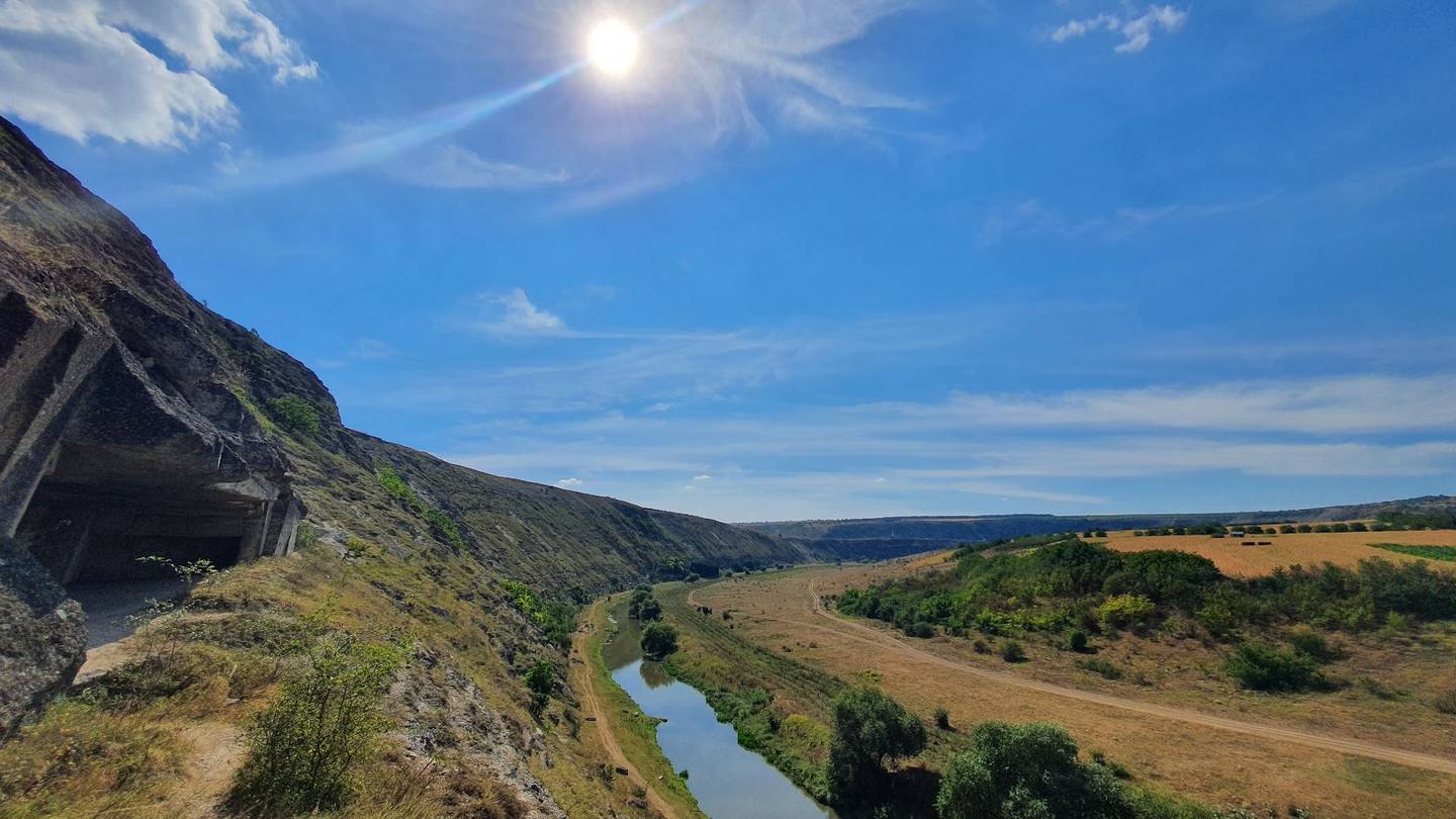 Panoramic river valley landscape with rocky clifftop and agricultural fields under clear sky