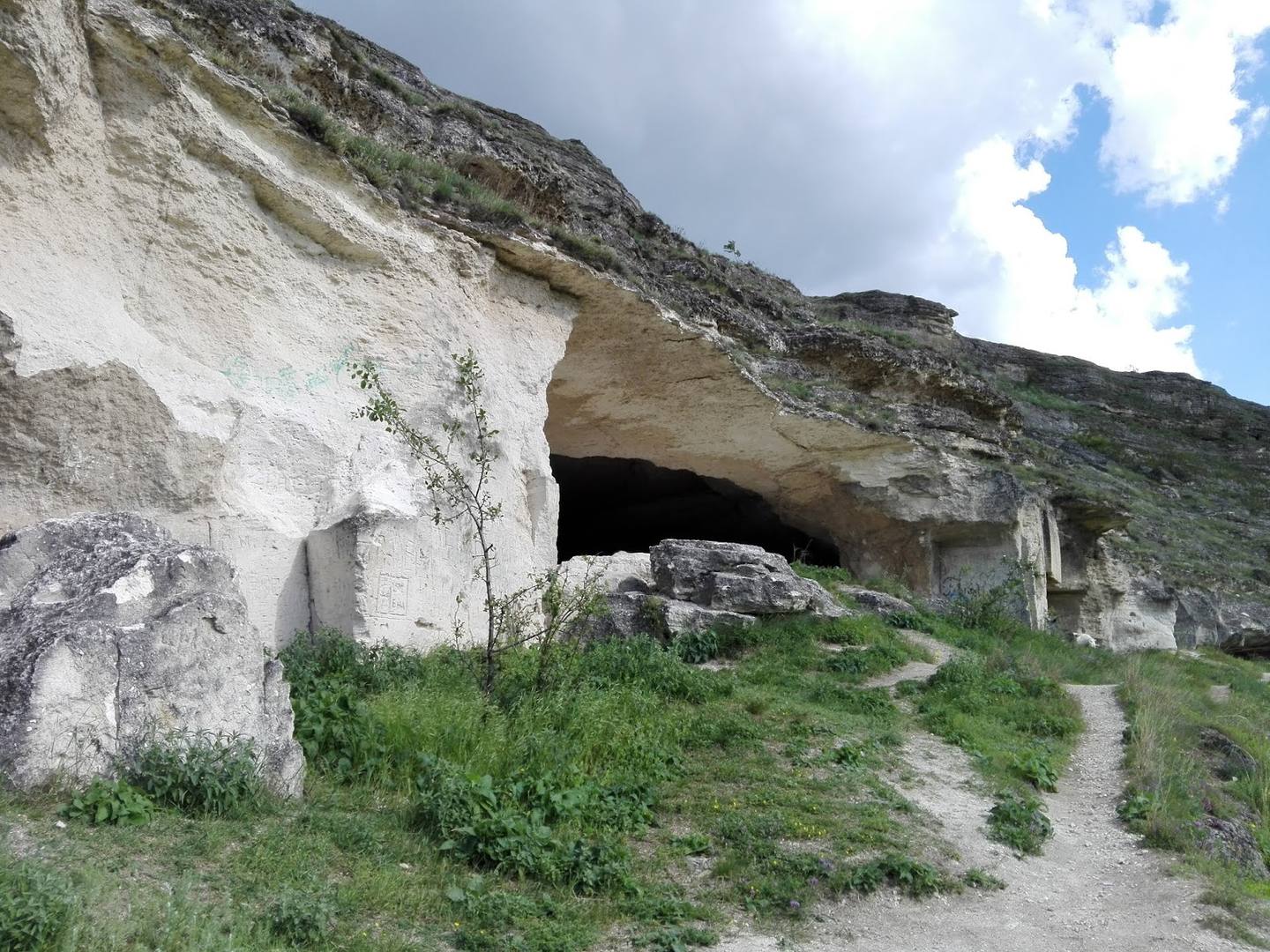 Historic stone fortress carved into cliff with natural cave entrance and overgrown vegetation