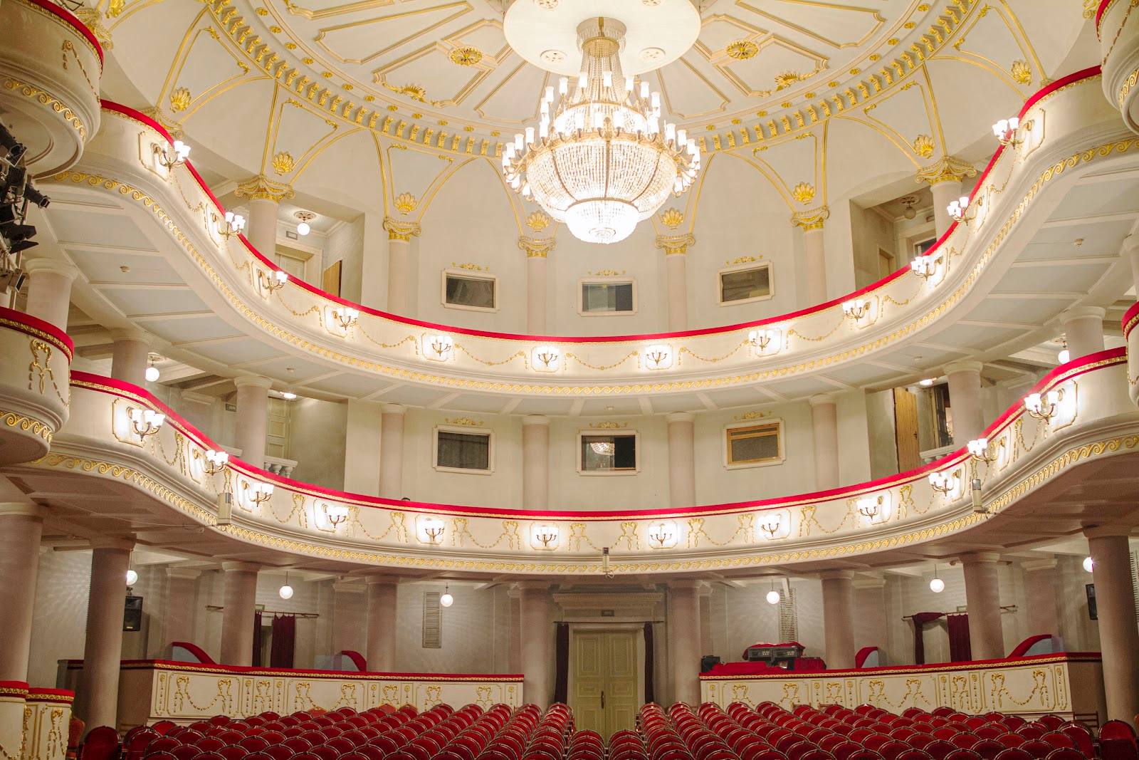 Historic theater interior with ornate ceiling, crystal chandelier, and red-upholstered balconies