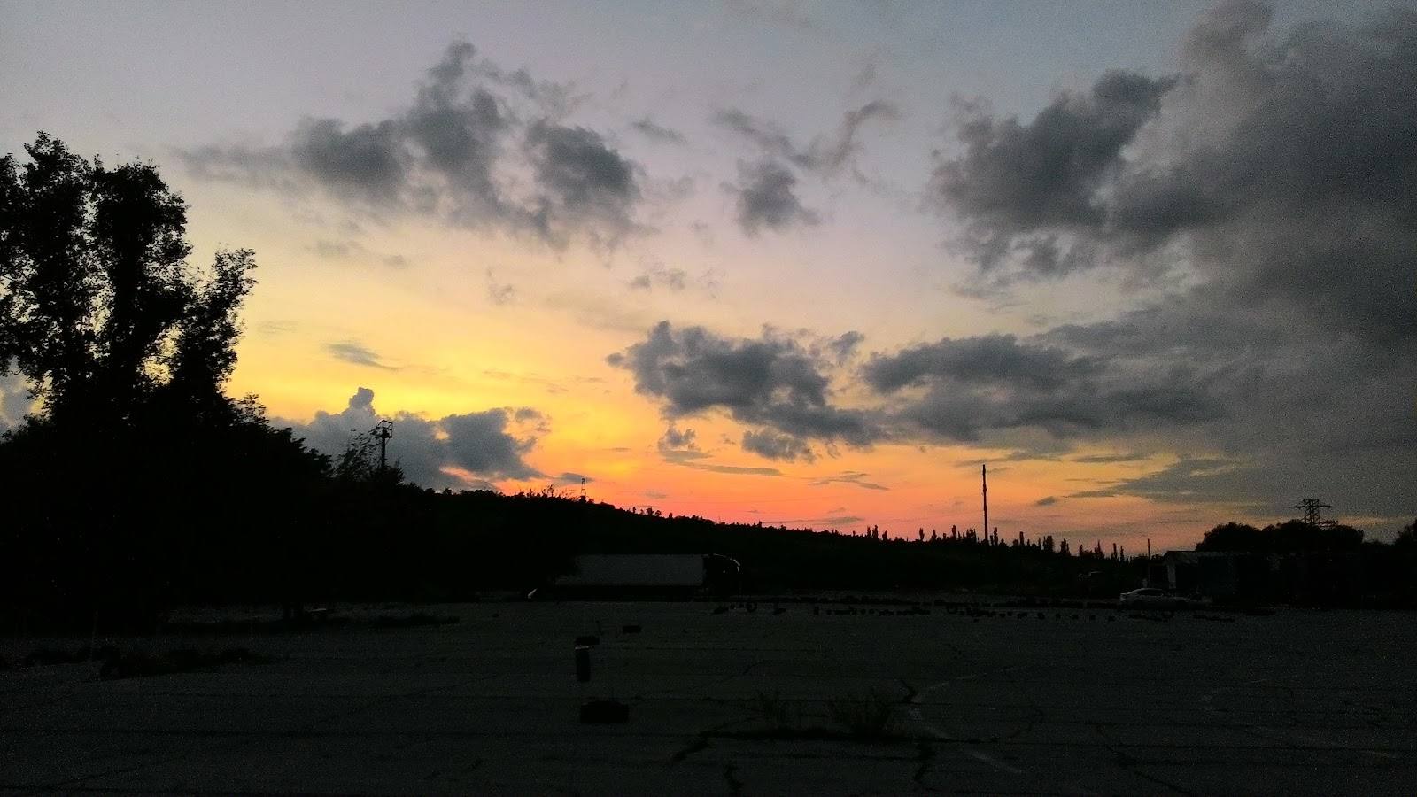 Sunset over water with silhouetted treeline and distant cityscape