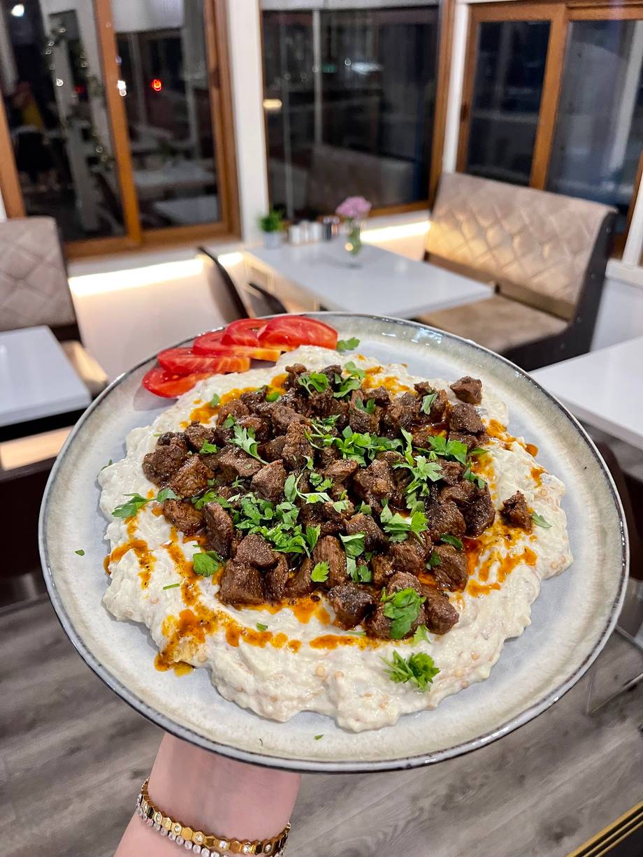 Hummus topped with seasoned meat and fresh herbs served at modern venue