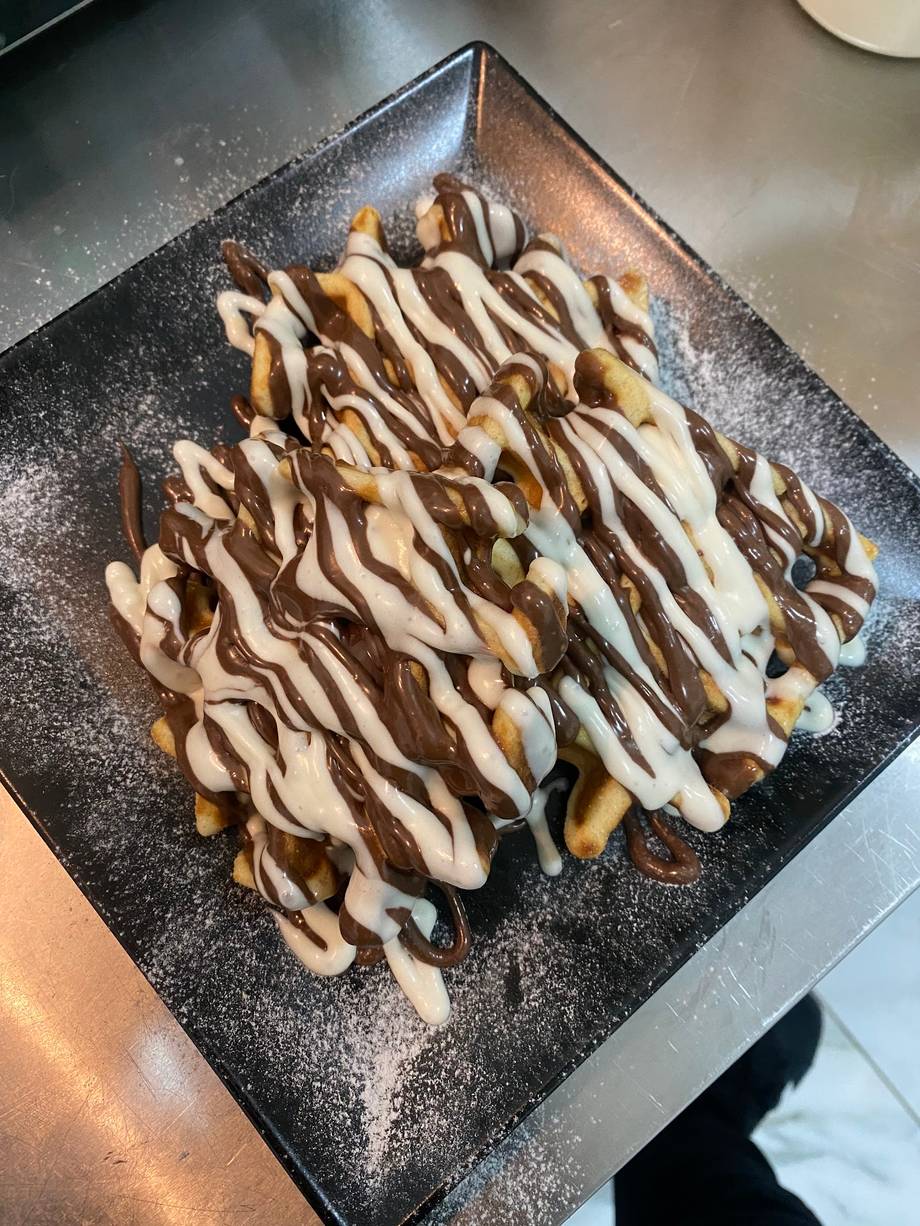 Chocolate and white sauce drizzled crepes or waffle dessert on black square plate