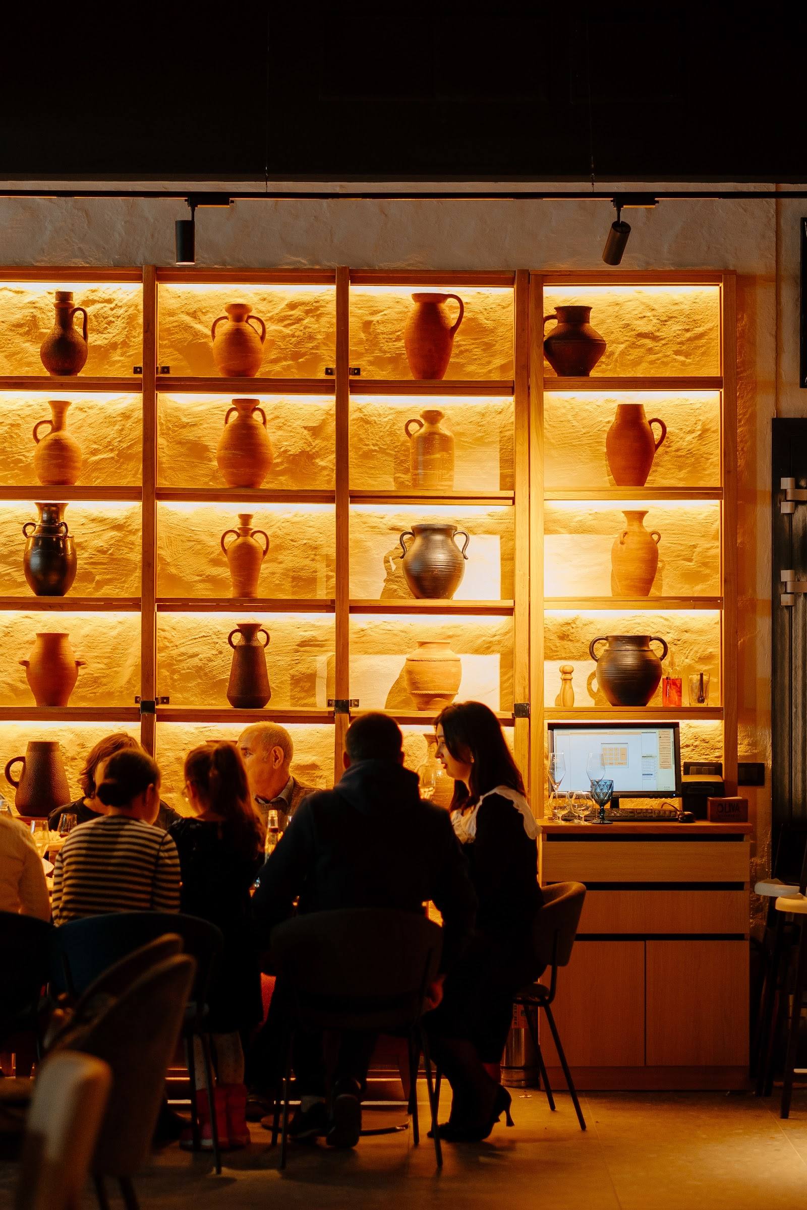 Illuminated wine display with terracotta vessels and guests seated at counter