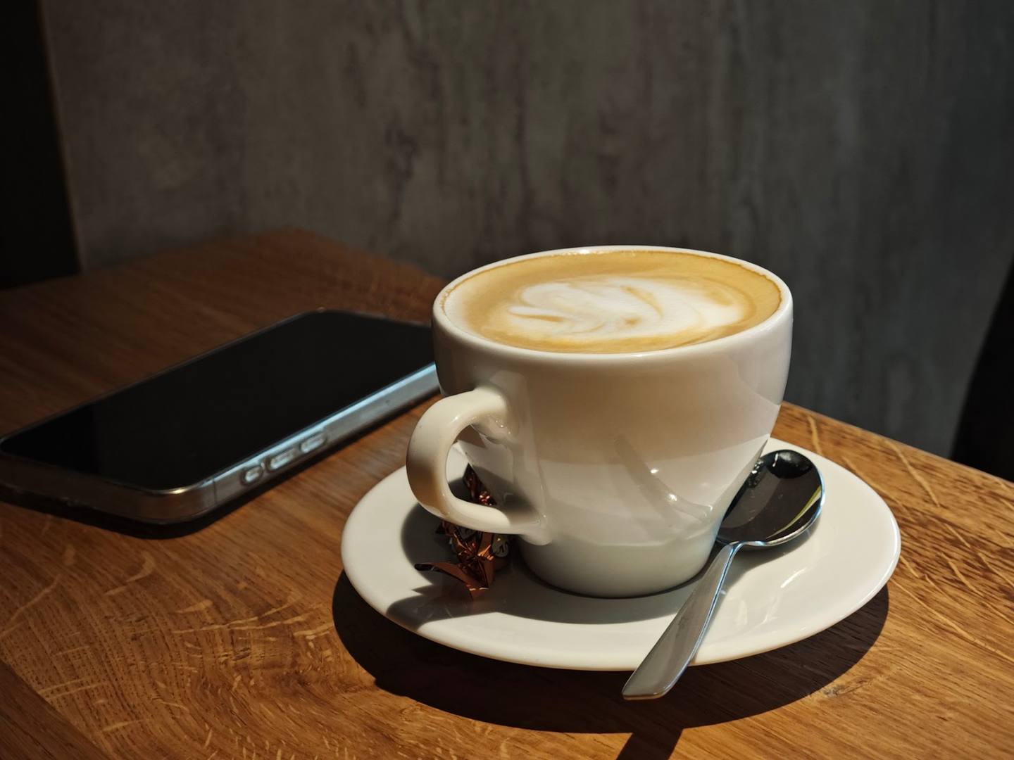 Cappuccino with latte art on wooden table near phone