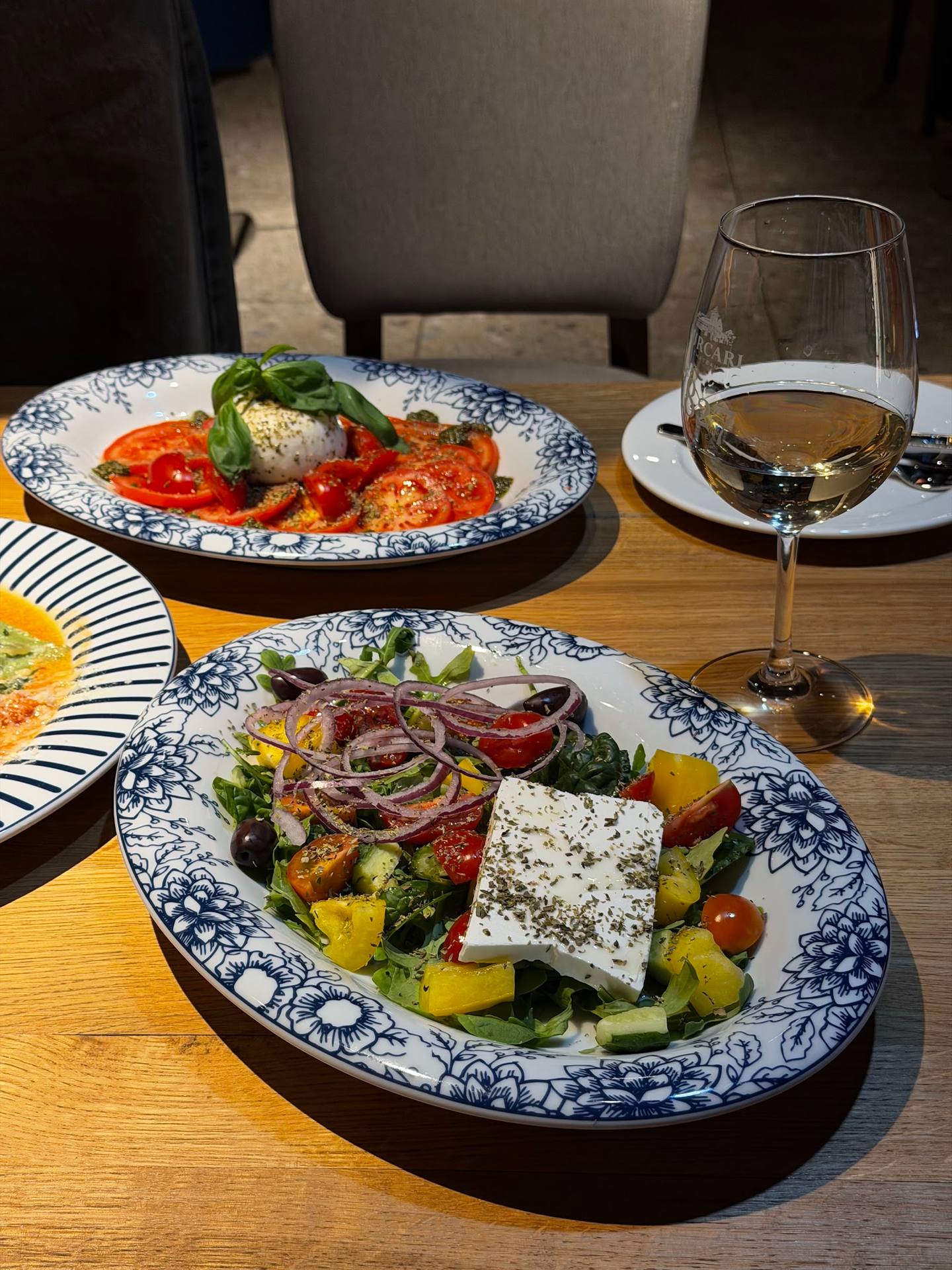 Plated Mediterranean salad and seafood dishes with white wine at restaurant table